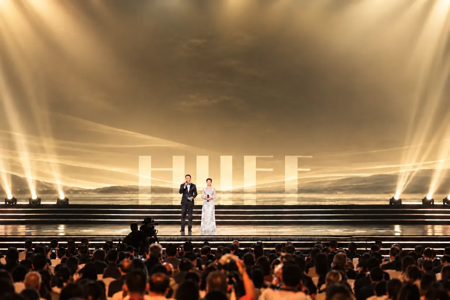 A warm yellow ceremony stage with a flat HIIFF screen, a host and the audience