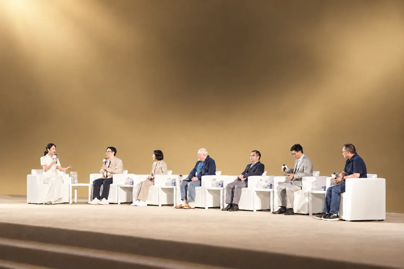 Seven guests in conversation on a bright, minimal warm yellow forum stage