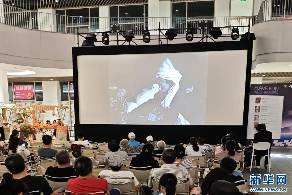 An open-air screening in the central plaza of Summer Station Mall, Sanya, at the 7th HIIFF, with the audience facing a large screen and the mall atrium behind